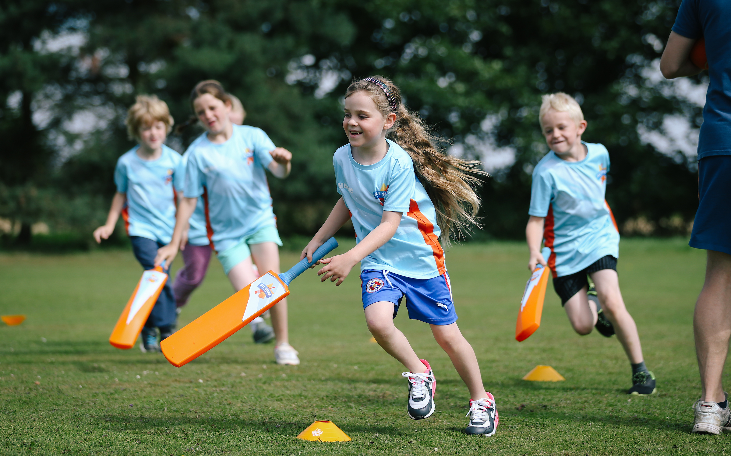 Four young children playing cricket. Wearing blue T shirts